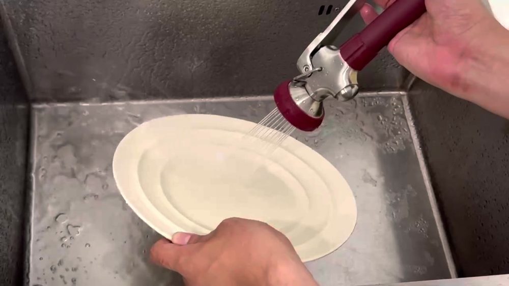 Achelous commercial pre-rinse spray head rinsing a plate at a stainless steel sink